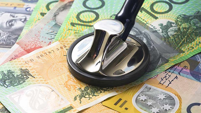 close-up of a stethoscope sitting on Australian money - how to save on health insurance lead image